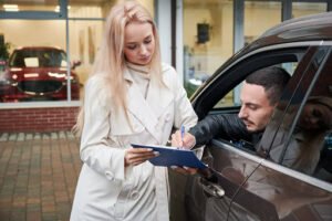 Woman signing a car rental agreement with an agent beside a vehicle.