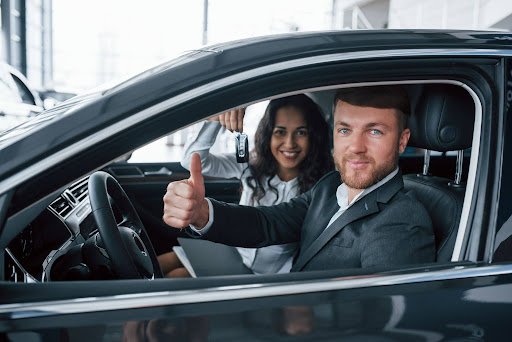 Luxury car rental customer receiving keys and giving thumbs up inside a premium vehicle